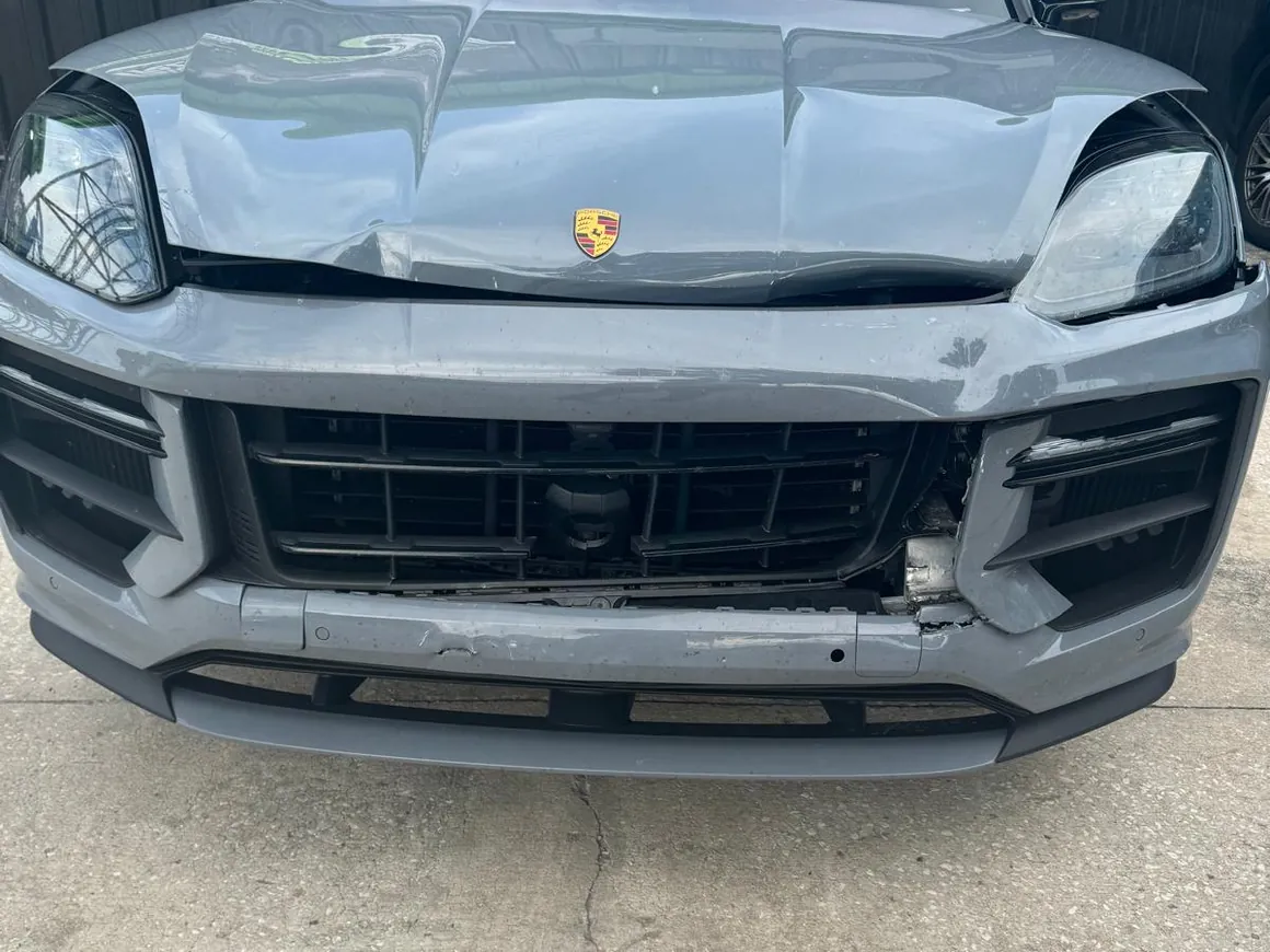 A grey Porsche Cayenne on intake, hood buckled and creased and the front bumper cracked and pulled away.